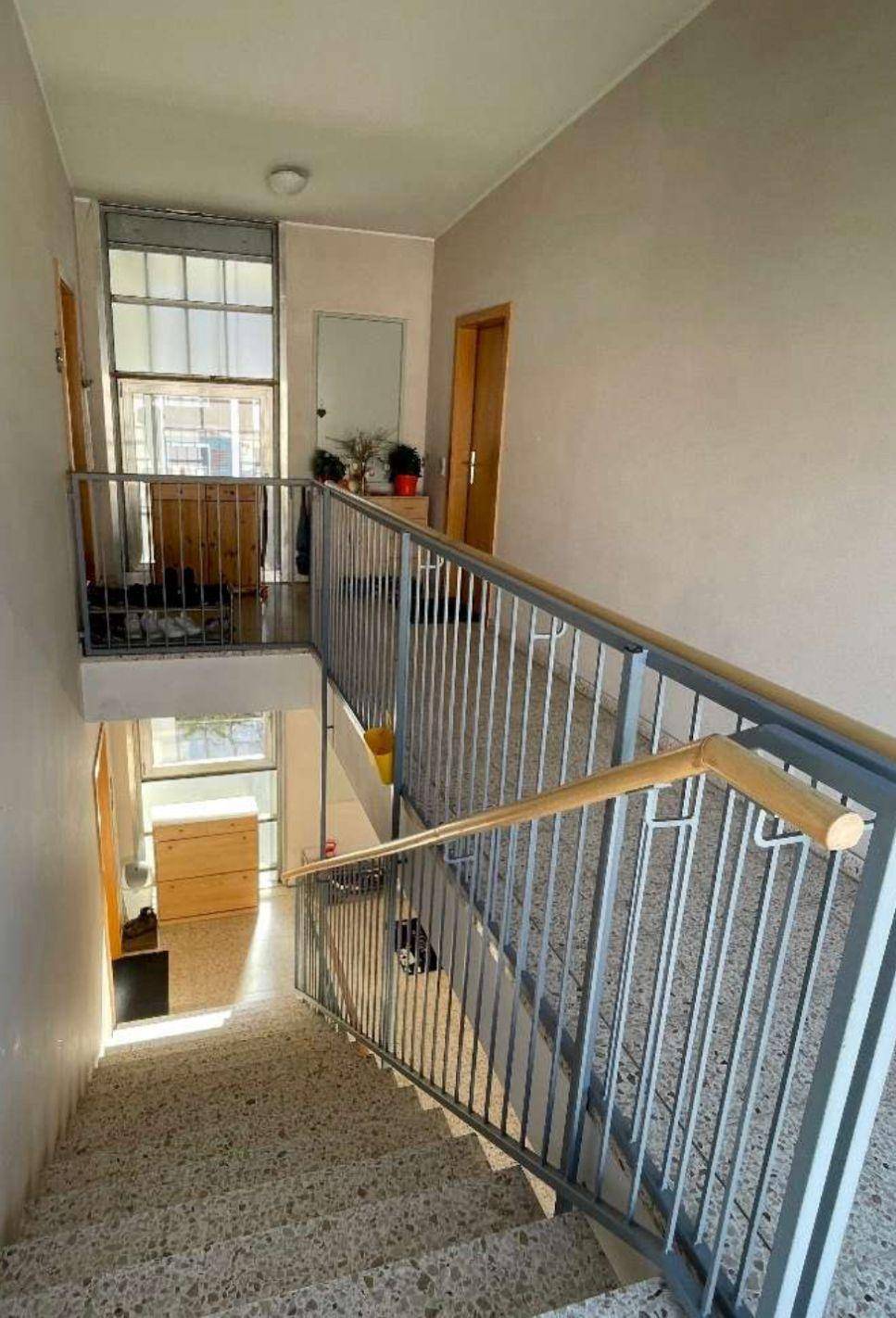 Helles Treppenhaus mit Terrazzoboden und Metallgeländer, das mehrere Etagen verbindet.