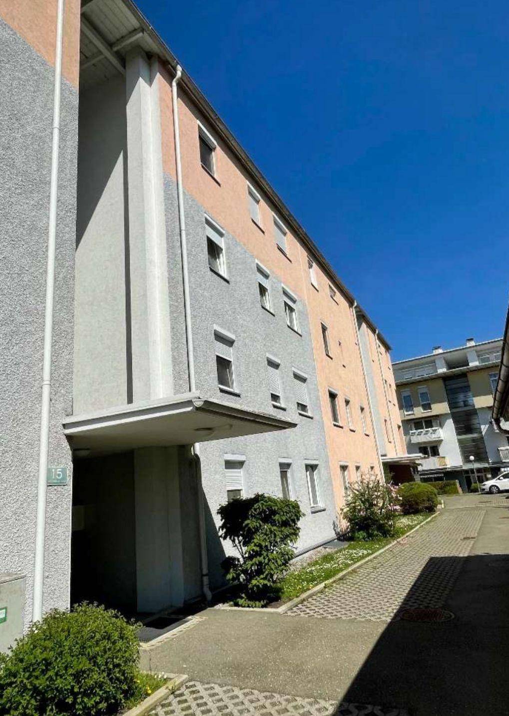Mehrfamilienhaus mit farbiger Fassade in Grau und Pfirsich sowie zahlreichen Fenstern.