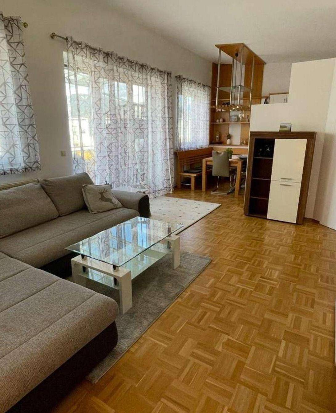 Gemütlicher Wohn- und Essbereich mit L-förmigem Sofa, Glastisch und Parkettboden.
