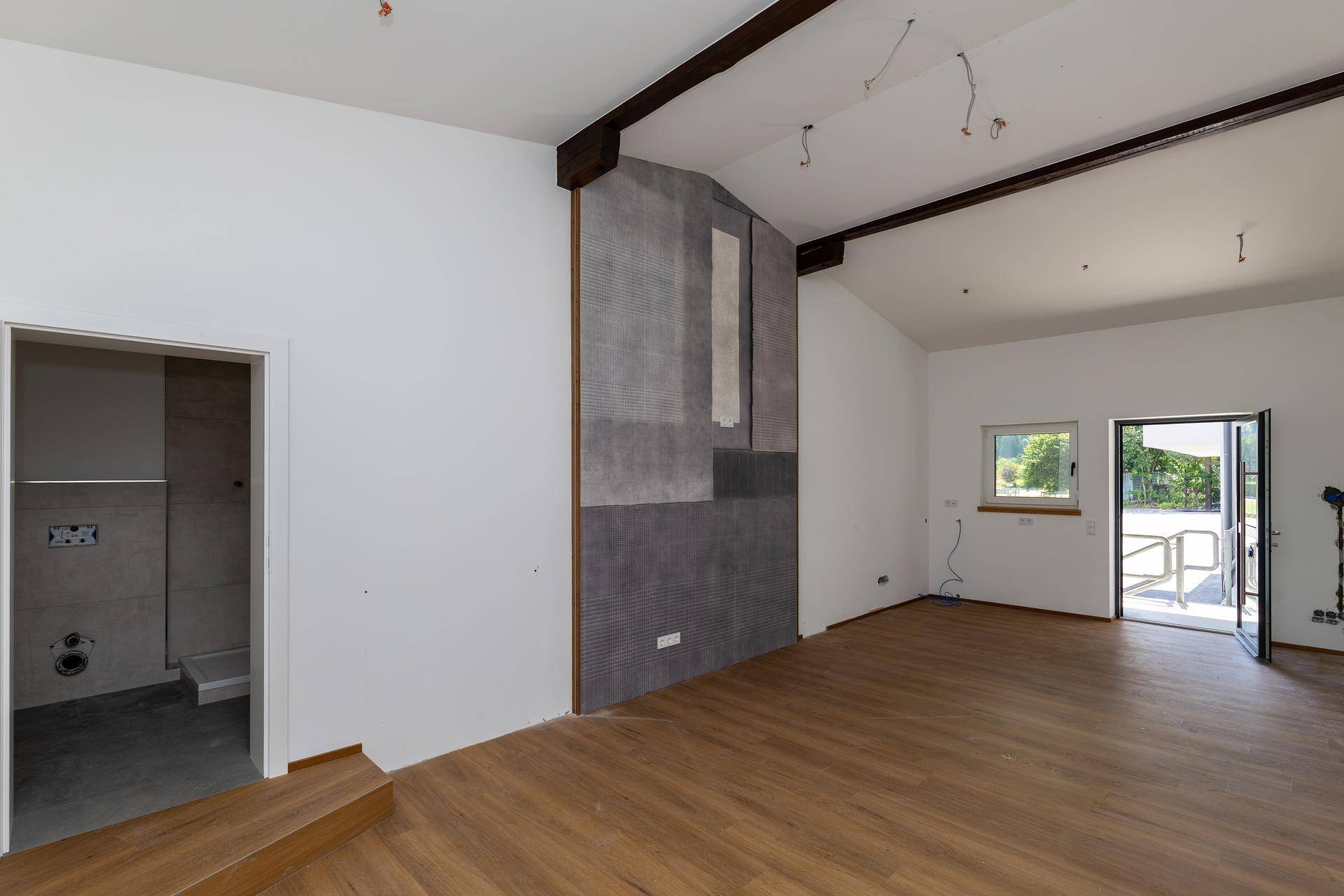 Geräumiger Raum mit Holzboden, sichtbaren Balken und einer gefliesten Akzentwand, mit Zugang nach draußen.