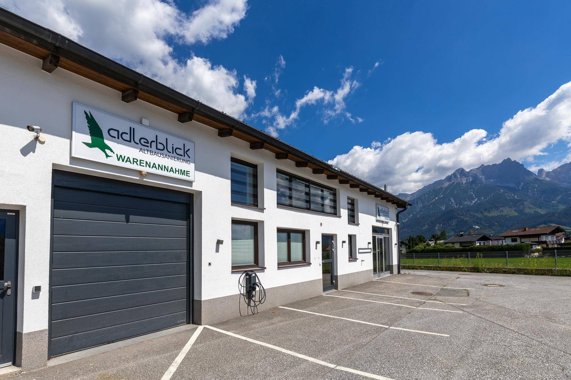 Gewerbegebäude mit großer Garageneinfahrt und Parkplätzen, umgeben von einer malerischen Berglandschaft.