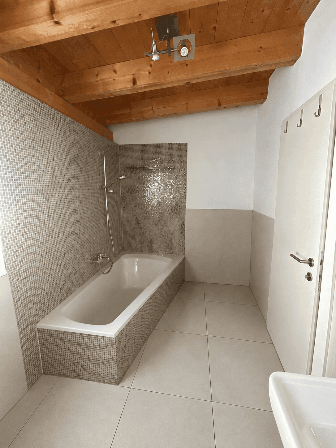 Modernes Badezimmer mit Badewanne, Mosaikfliesen und sichtbarer Holzbalkendecke.