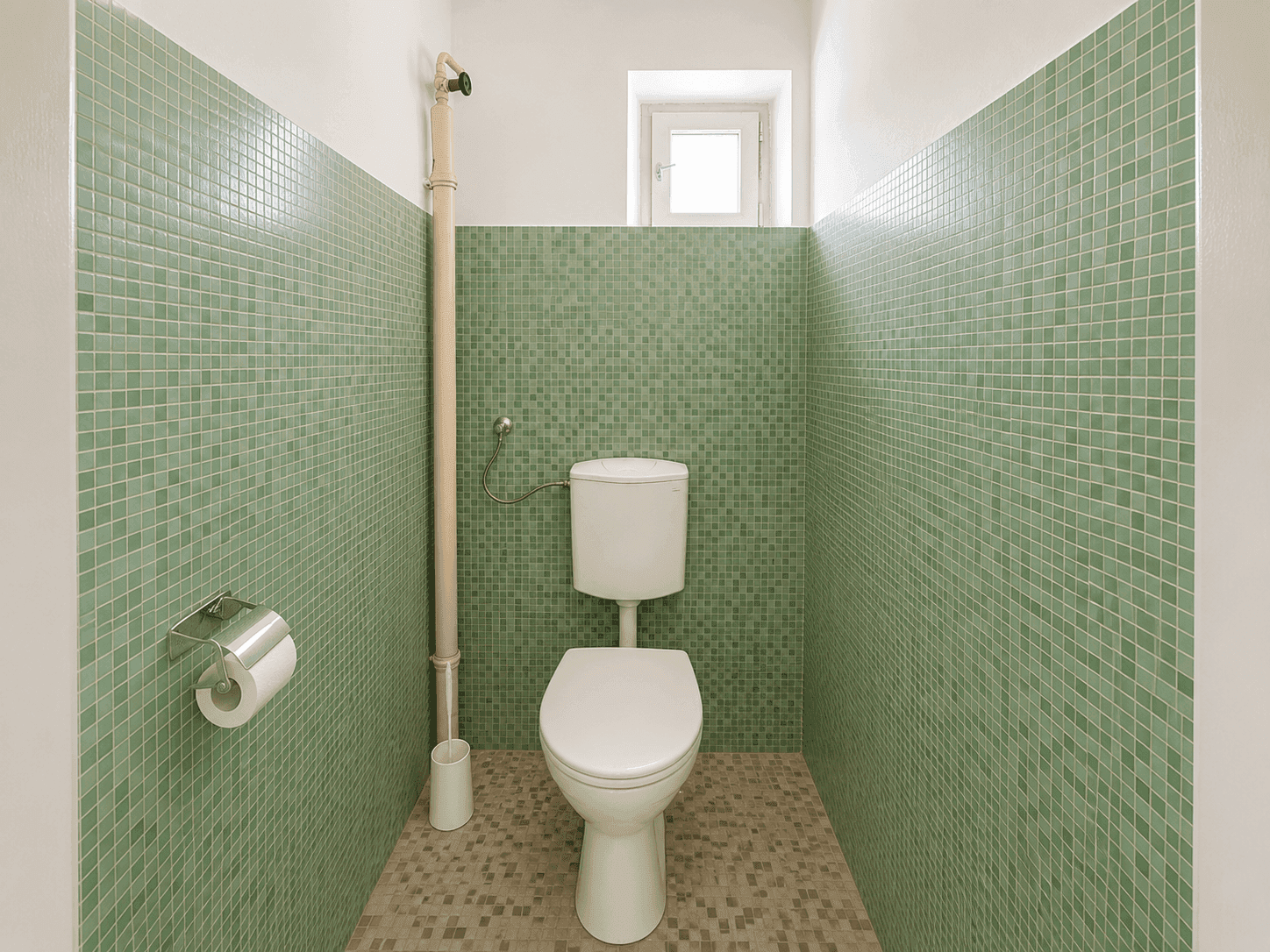 Separates WC mit grünen Mosaikfliesen und kleinem Fenster für Belüftung.