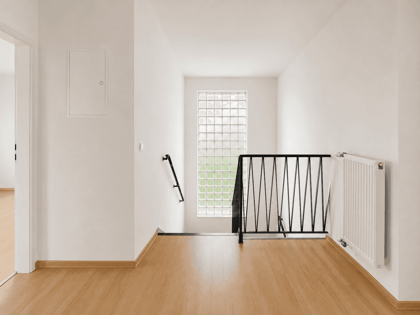 Oberer Flurbereich mit Holzfußboden und Treppengeländer, hell durch Glasbausteinfenster.