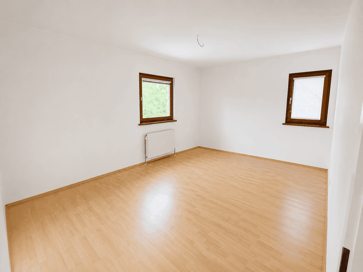 Leeres Zimmer mit Laminatboden und zwei Fenstern, ideal als Schlaf- oder Arbeitszimmer.