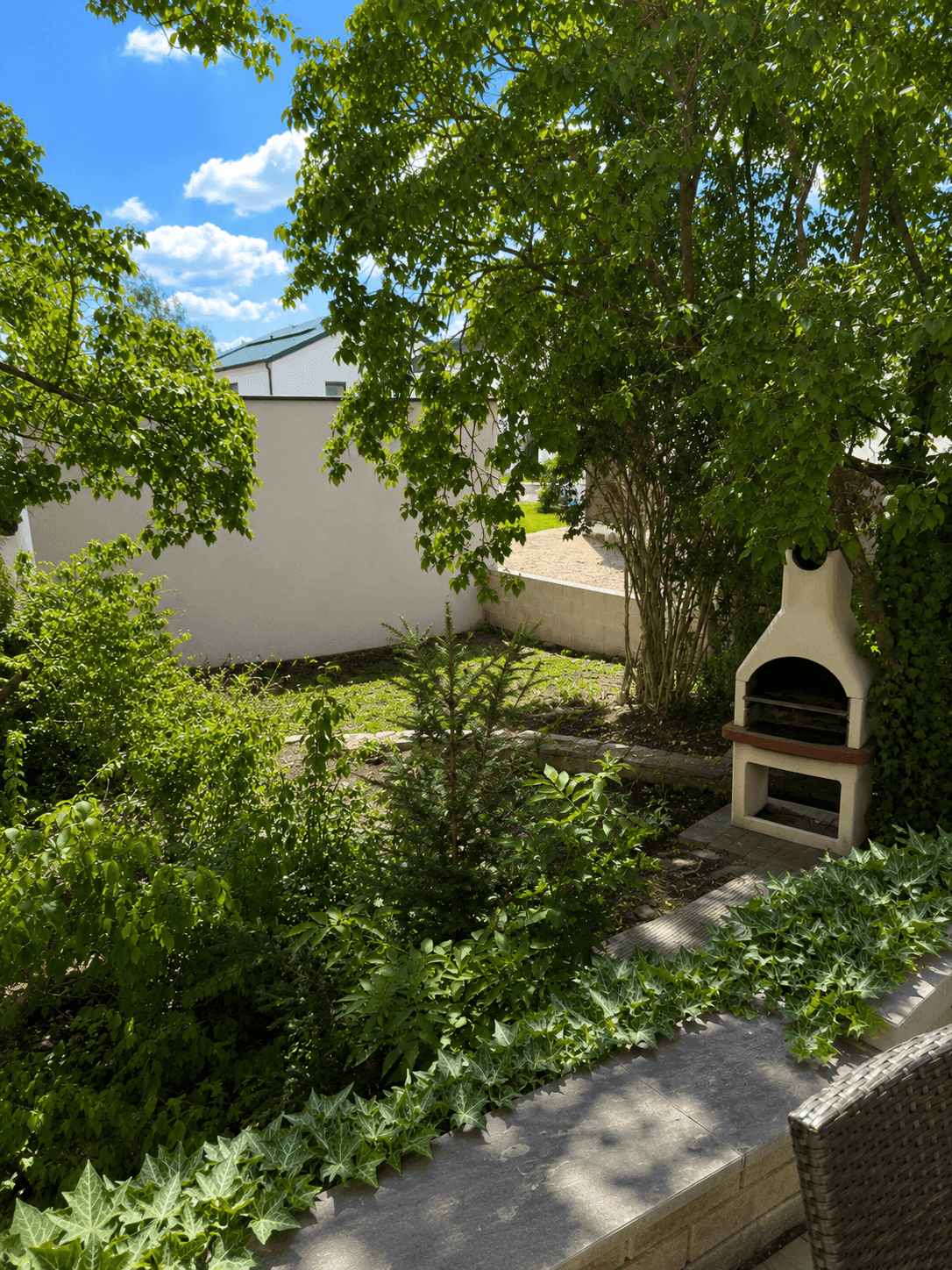 Grüner Gartenbereich mit integriertem Grillplatz, umgeben von Bäumen und Sträuchern.