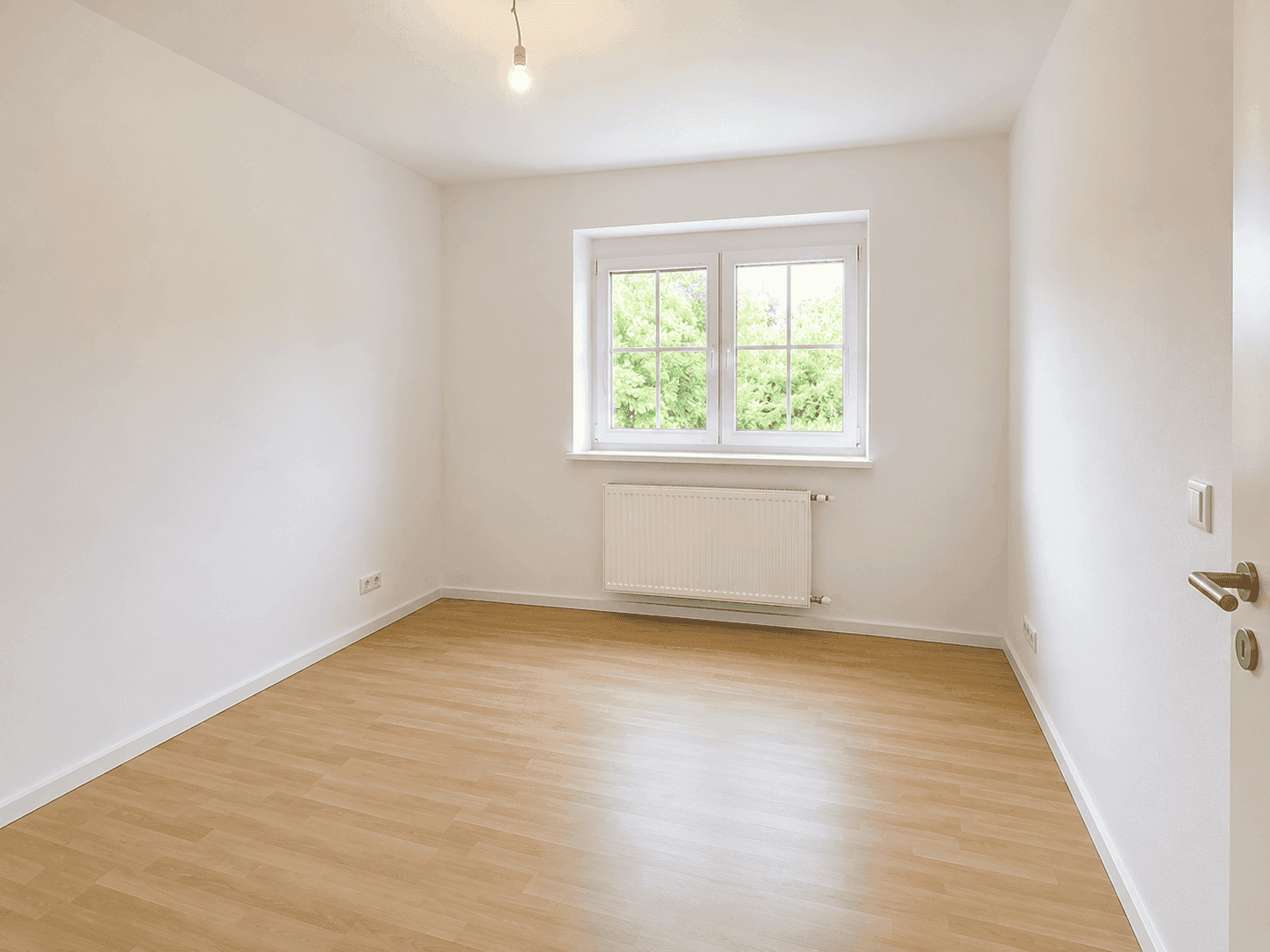 Freundliches Zimmer mit Laminatboden und Fensterblick ins Grüne, ideal als Schlafzimmer.