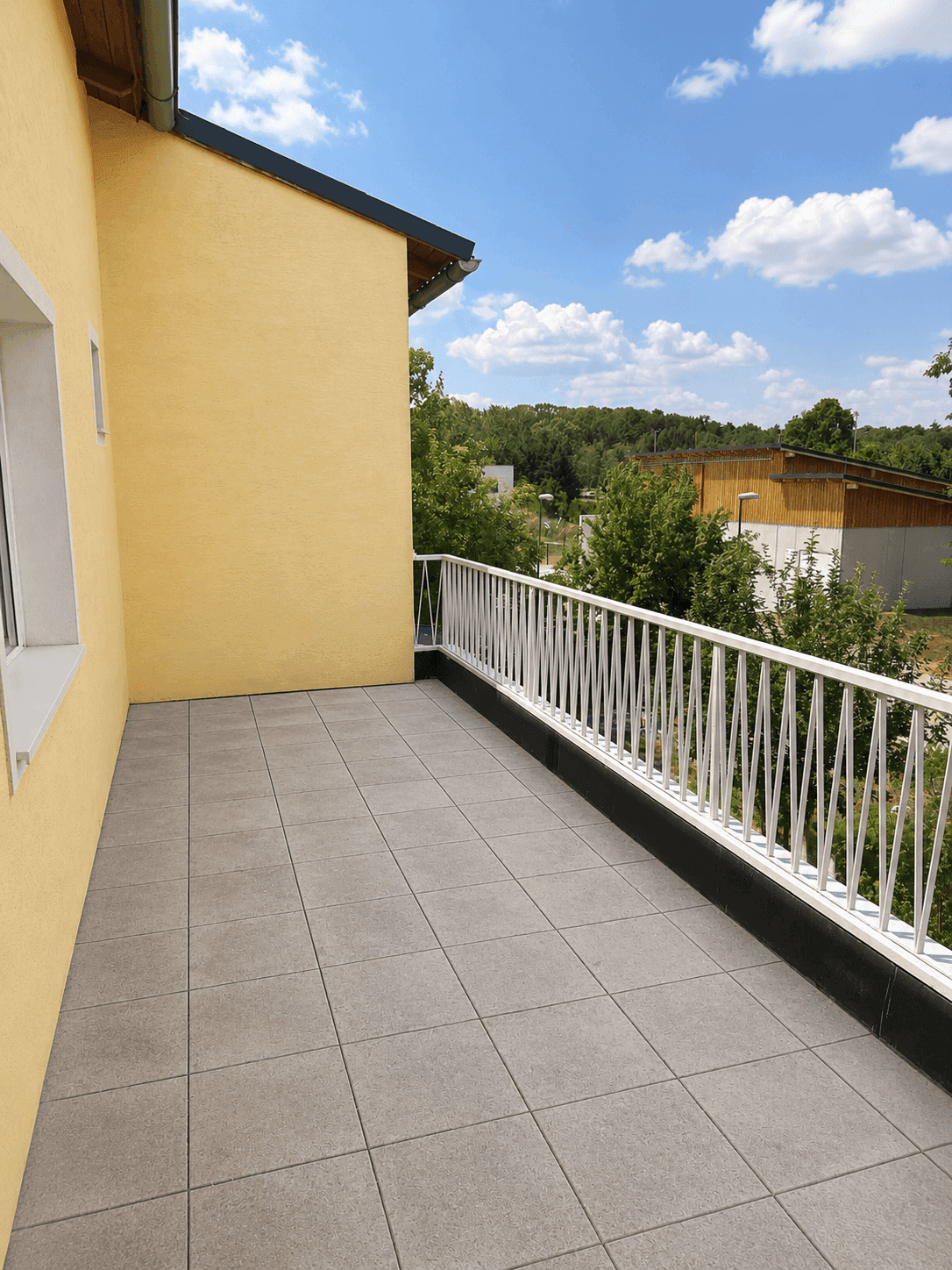Gefliester Balkon mit weißem Geländer und weitem Blick in die Umgebung.