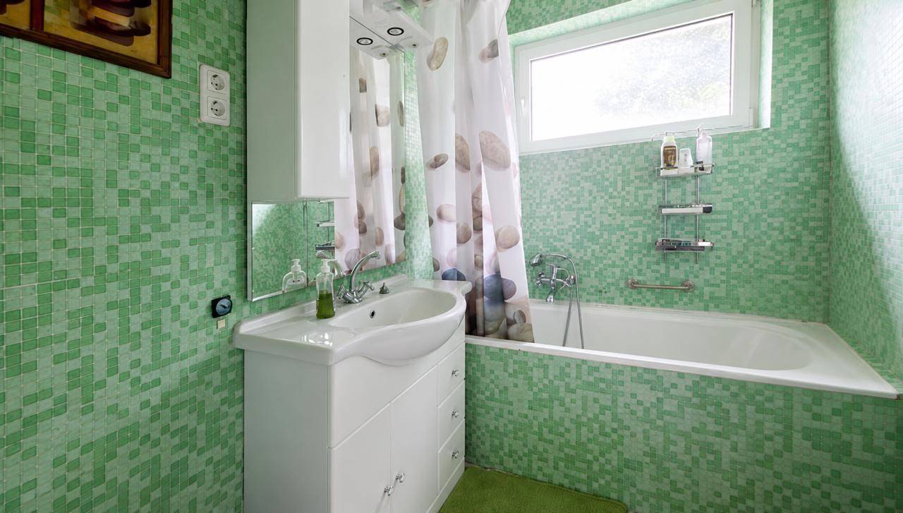 Badezimmer mit grünen Mosaikfliesen, Badewanne und Fenster für Tageslicht.