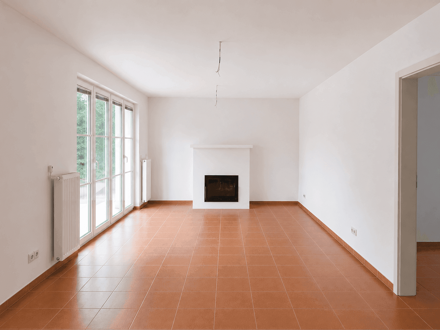 Geräumiges Wohnzimmer mit Kamin und Terracottaboden, bereit für individuelle Gestaltung.