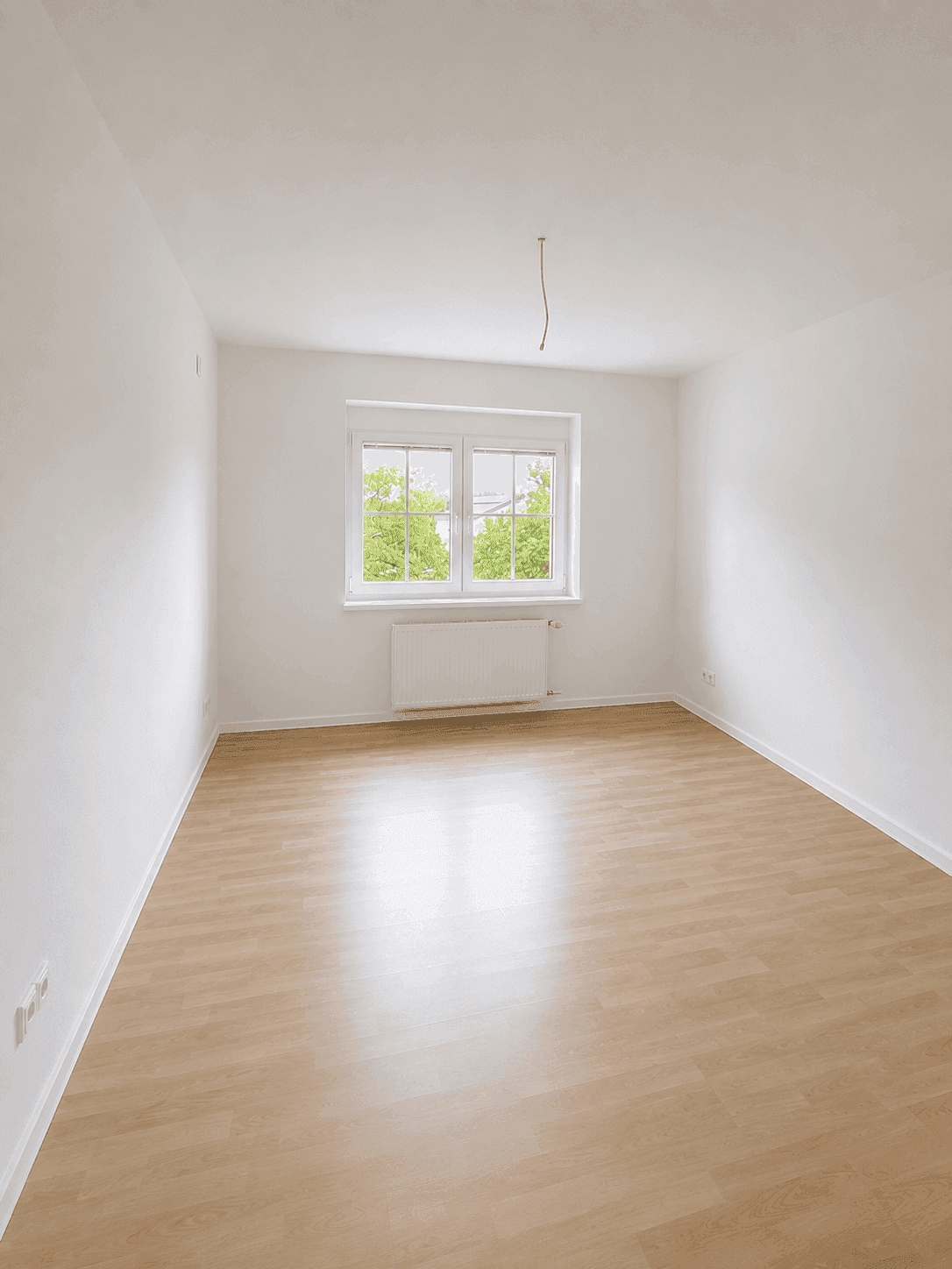 Helles Zimmer mit Laminatboden und großem Fenster, vielseitig nutzbar.