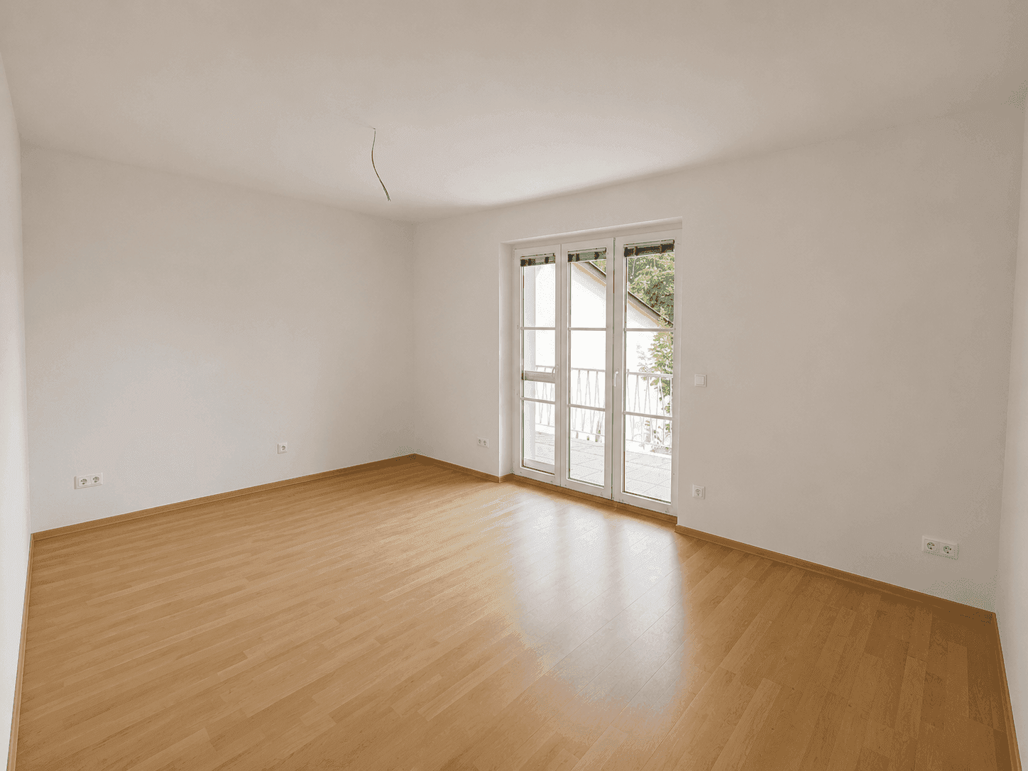 Geräumiges Zimmer mit Laminatboden und Zugang zu einem französischen Balkon.