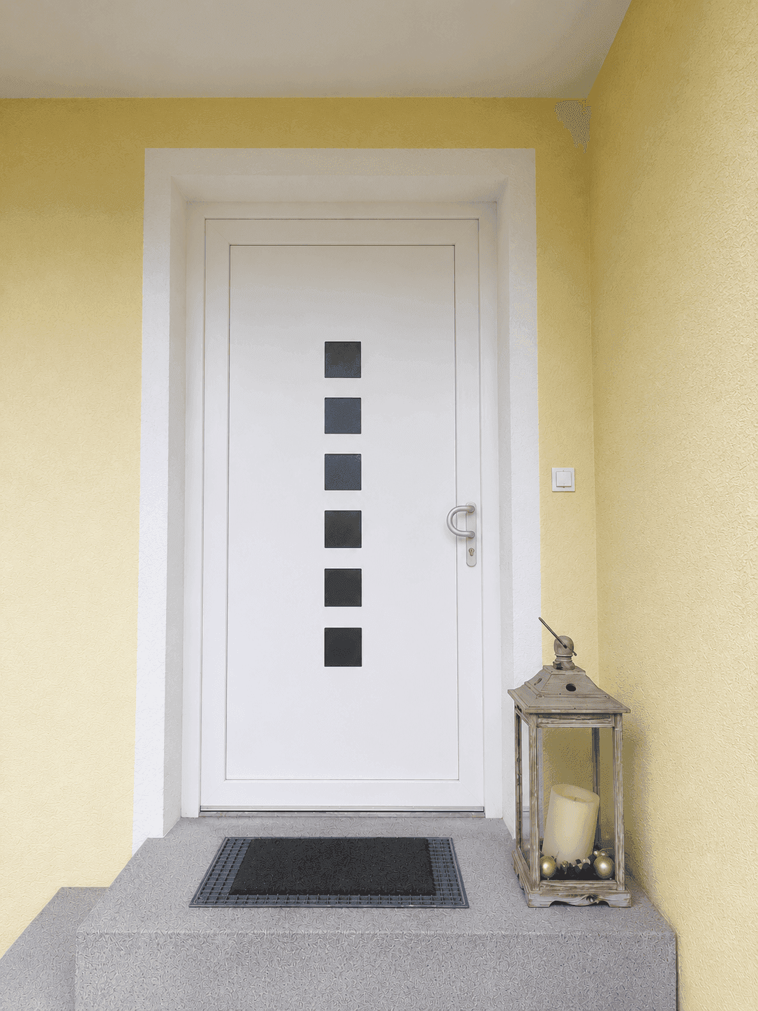 Moderner Hauseingang mit weißer Tür und dekorativer Laterne, einladend gestaltet.