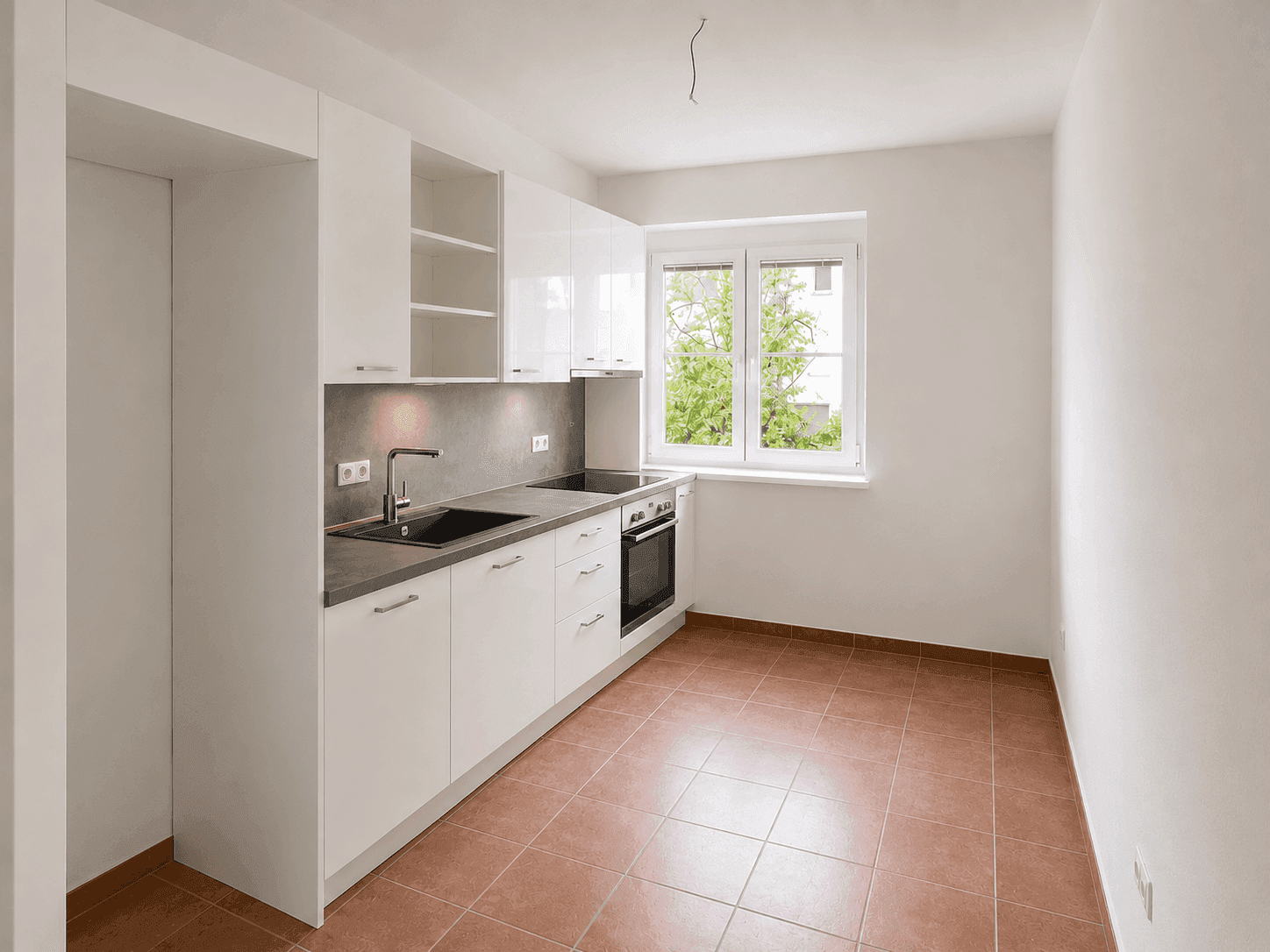 Moderne Einbauküche mit weißen Hochglanzfronten, integriertem Backofen und Fensterblick ins Grüne.