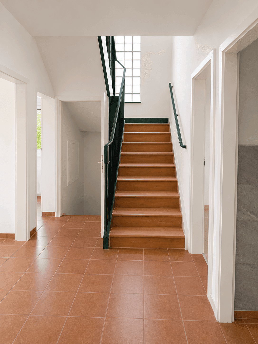 Heller Flur mit Holztreppe und Glasbausteinfenster, verbindet die verschiedenen Etagen.