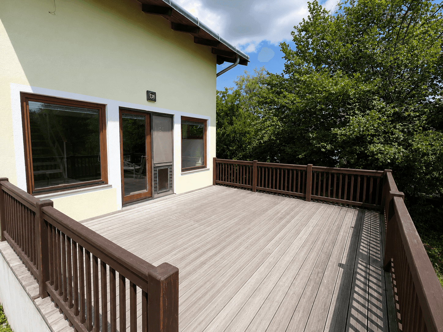 Große Holzterrasse am Haus mit Blick auf die umliegende grüne Natur.