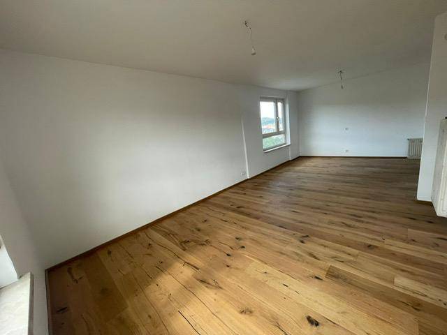 Geräumiges, helles Zimmer mit Holzboden und einem Fenster, das viel Tageslicht hereinlässt.