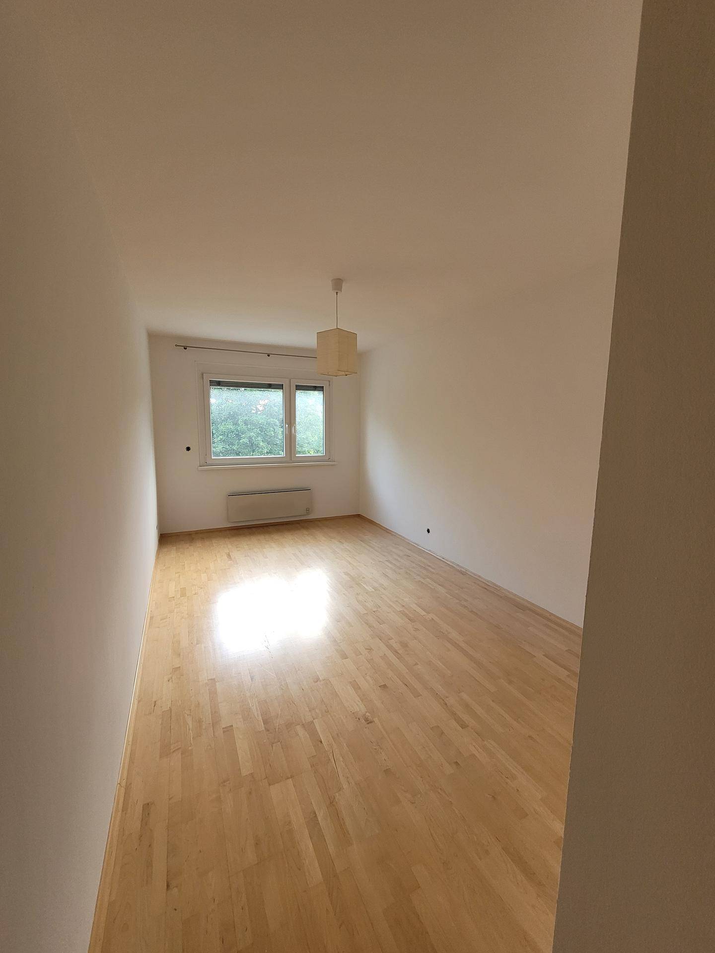 Helles Schlafzimmer mit Holzparkettboden und Fenster mit Blick ins Grüne.