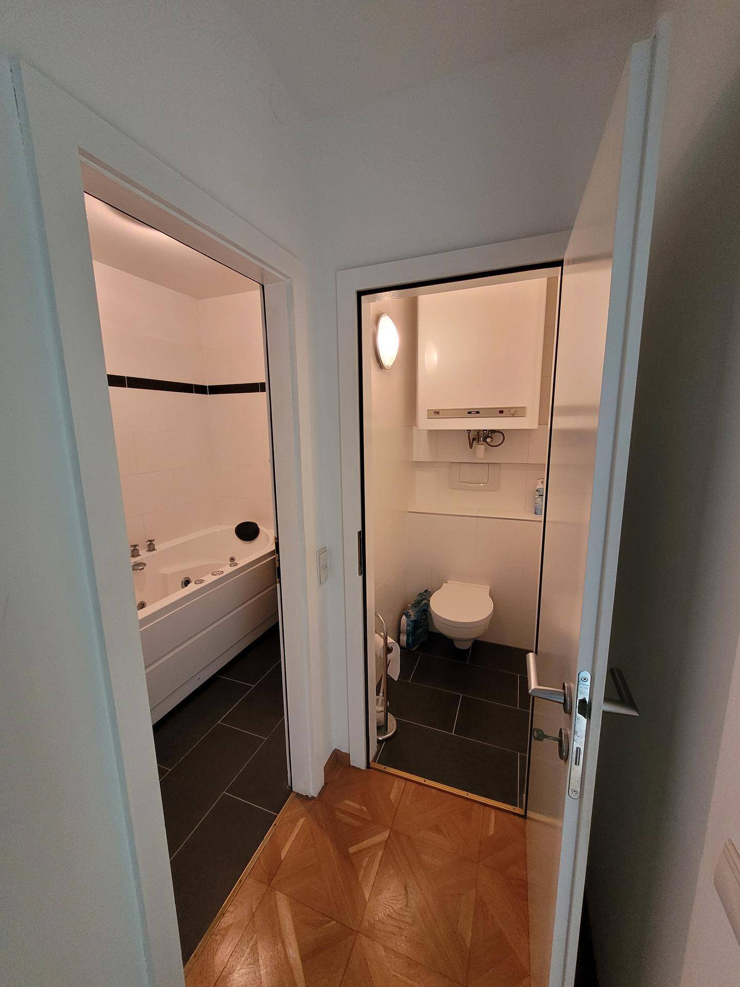 Flur mit Zugang zu einem Badezimmer mit Badewanne und einer separaten Toilette.