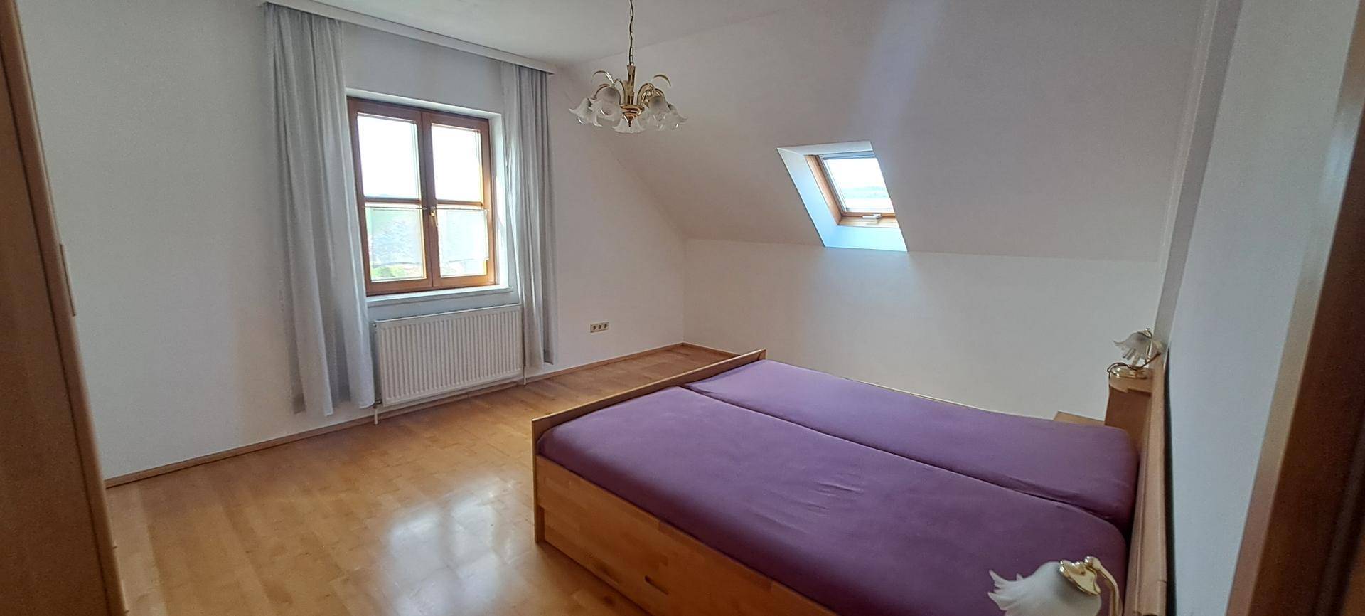 Helles Schlafzimmer im Dachgeschoss mit Holzboden, Dachfenster und Doppelbett.