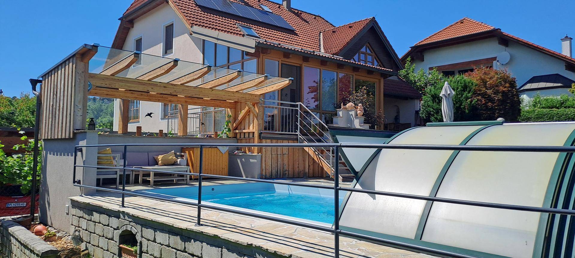 Hausfassade mit Poolbereich, Überdachung und Blick auf die umliegende Landschaft.