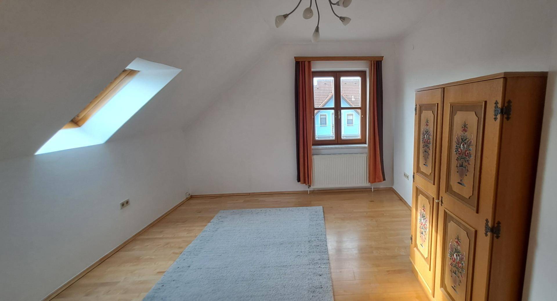 Geräumiges Schlafzimmer im Dachgeschoss mit Holzboden, Dachfenster und traditionellem Schrank.