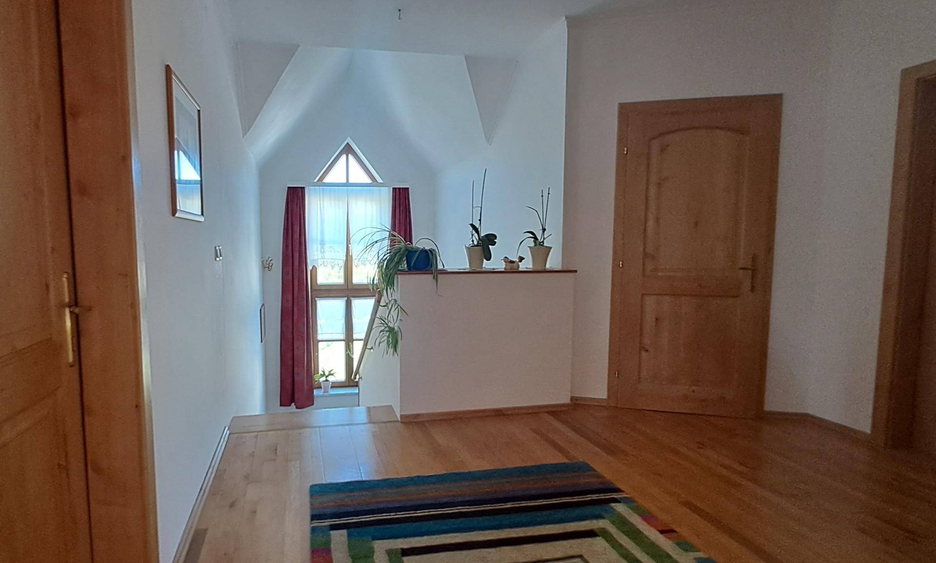Heller Flur im Dachgeschoss mit Holzboden und Blick auf das Giebelfenster.