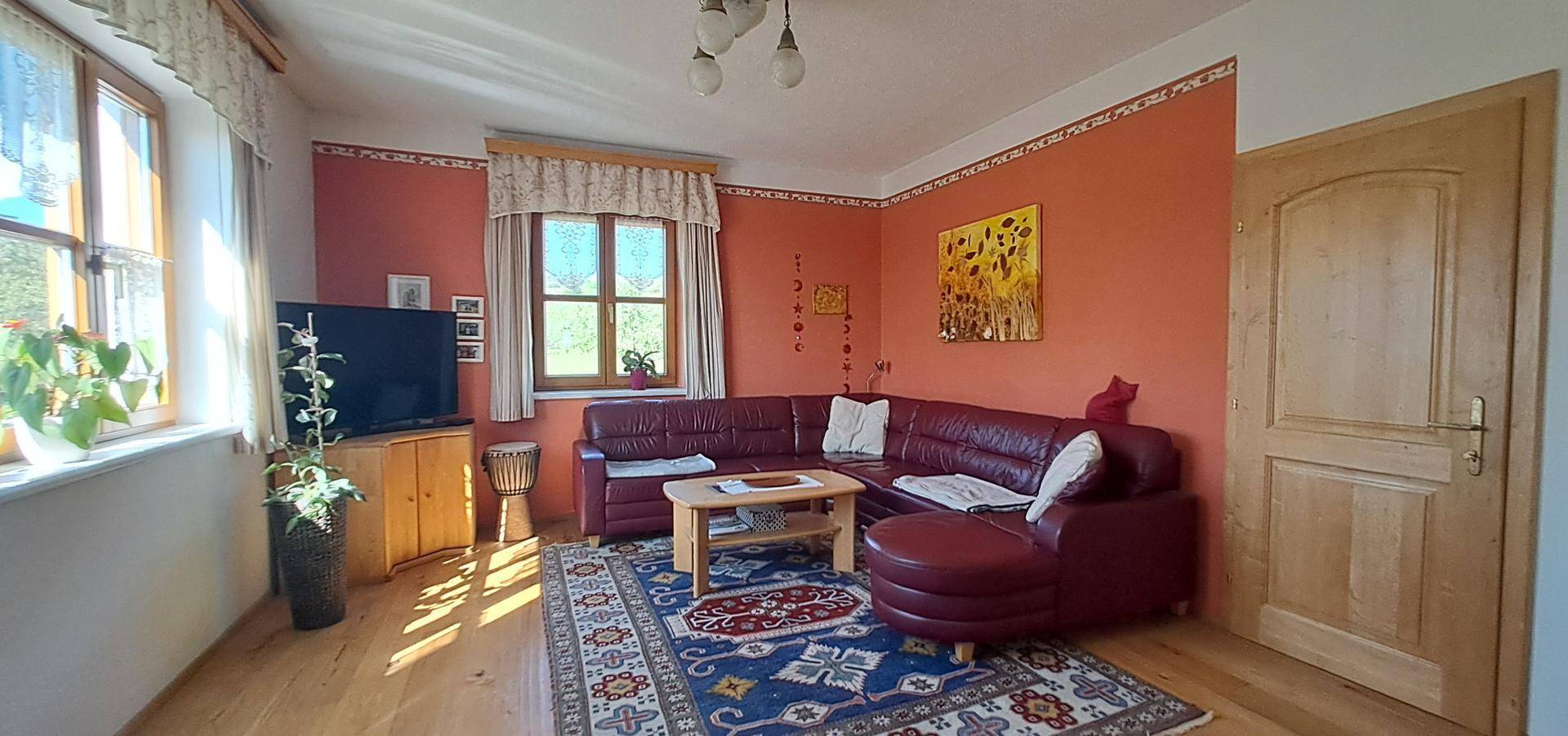 Gemütliches Wohnzimmer mit rotem Ecksofa, Holzboden und traditionellem Teppich.