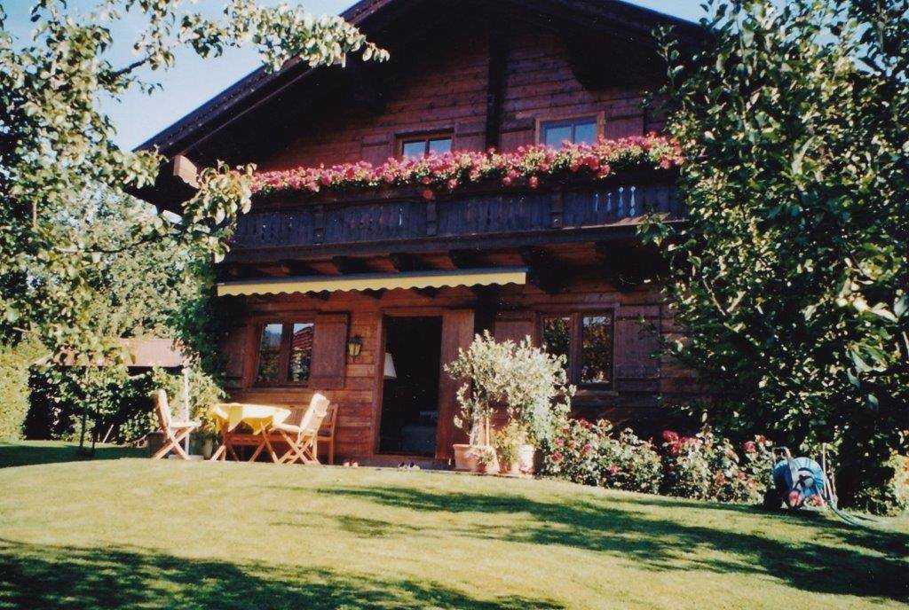 Traditionelles Holzhaus mit blühendem Balkon, sonniger Terrasse und gepflegtem Garten.