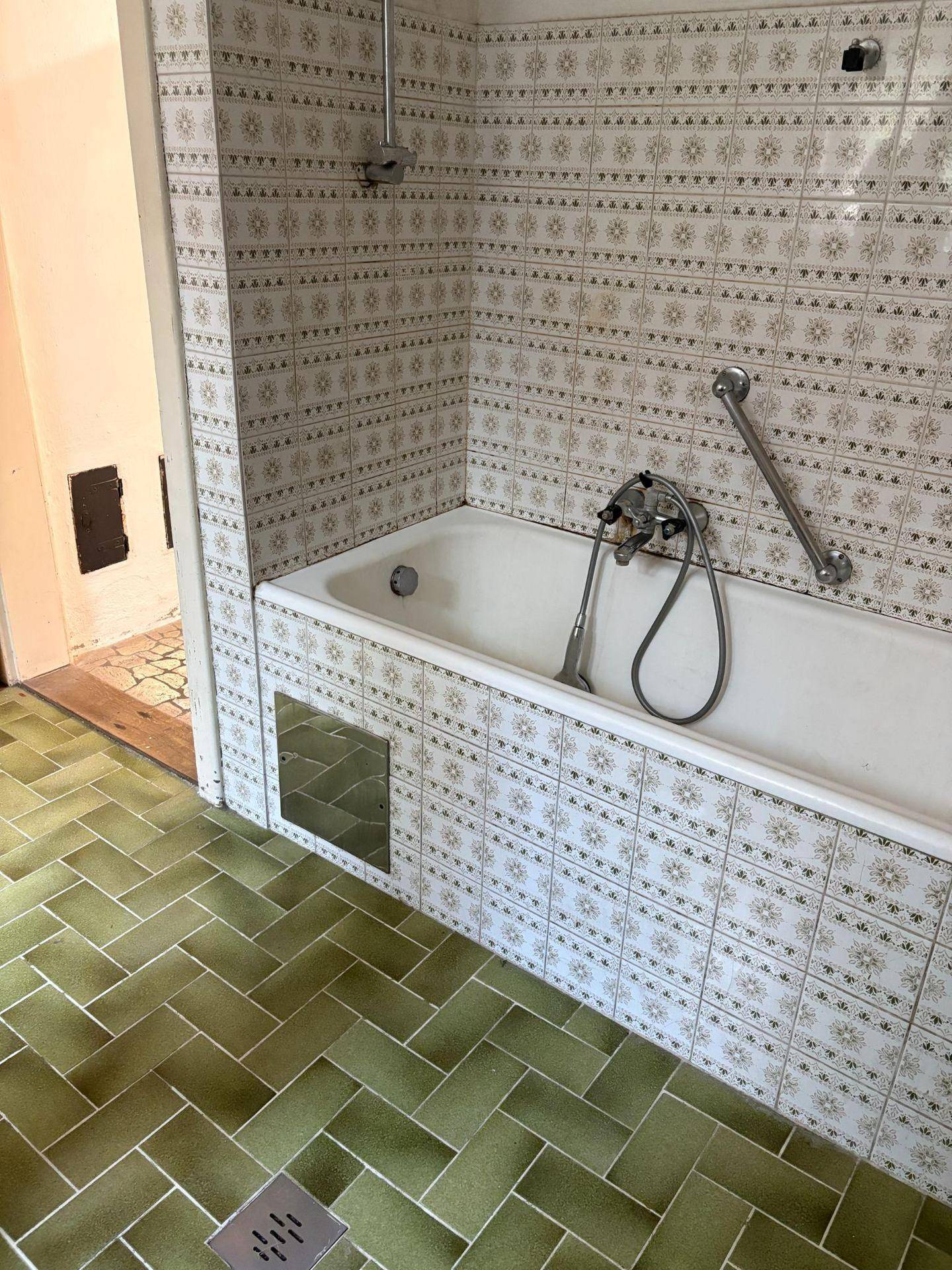 Badezimmer mit Badewanne, grünen Fliesen und Haltegriffen an der Wand.