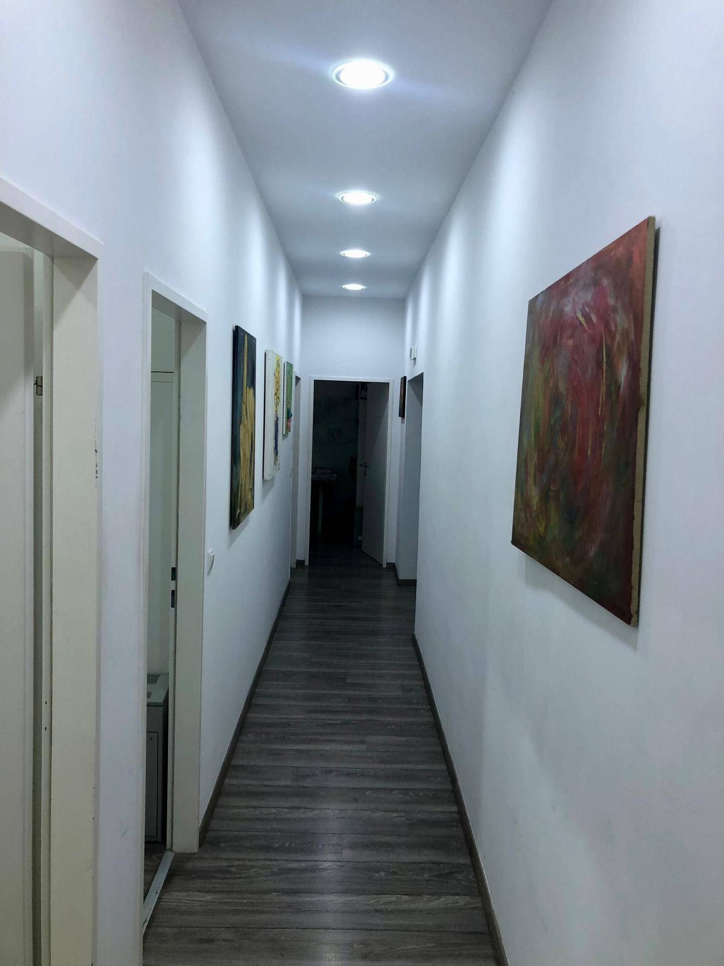 Langer, schmaler Flur mit Einbaustrahlern in der Decke und Kunstwerken an den weißen Wänden.