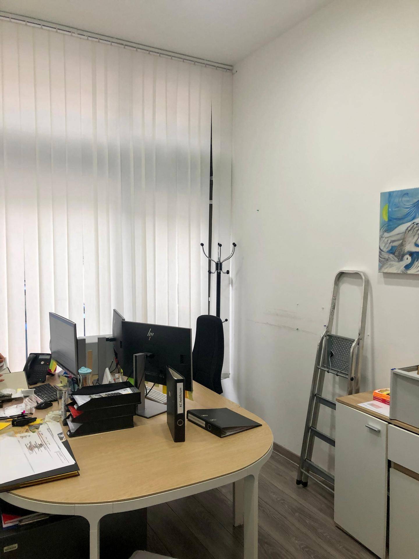 Büroarbeitsplatz mit Schreibtisch, Computermonitoren und vertikalen Jalousien am großen Fenster.