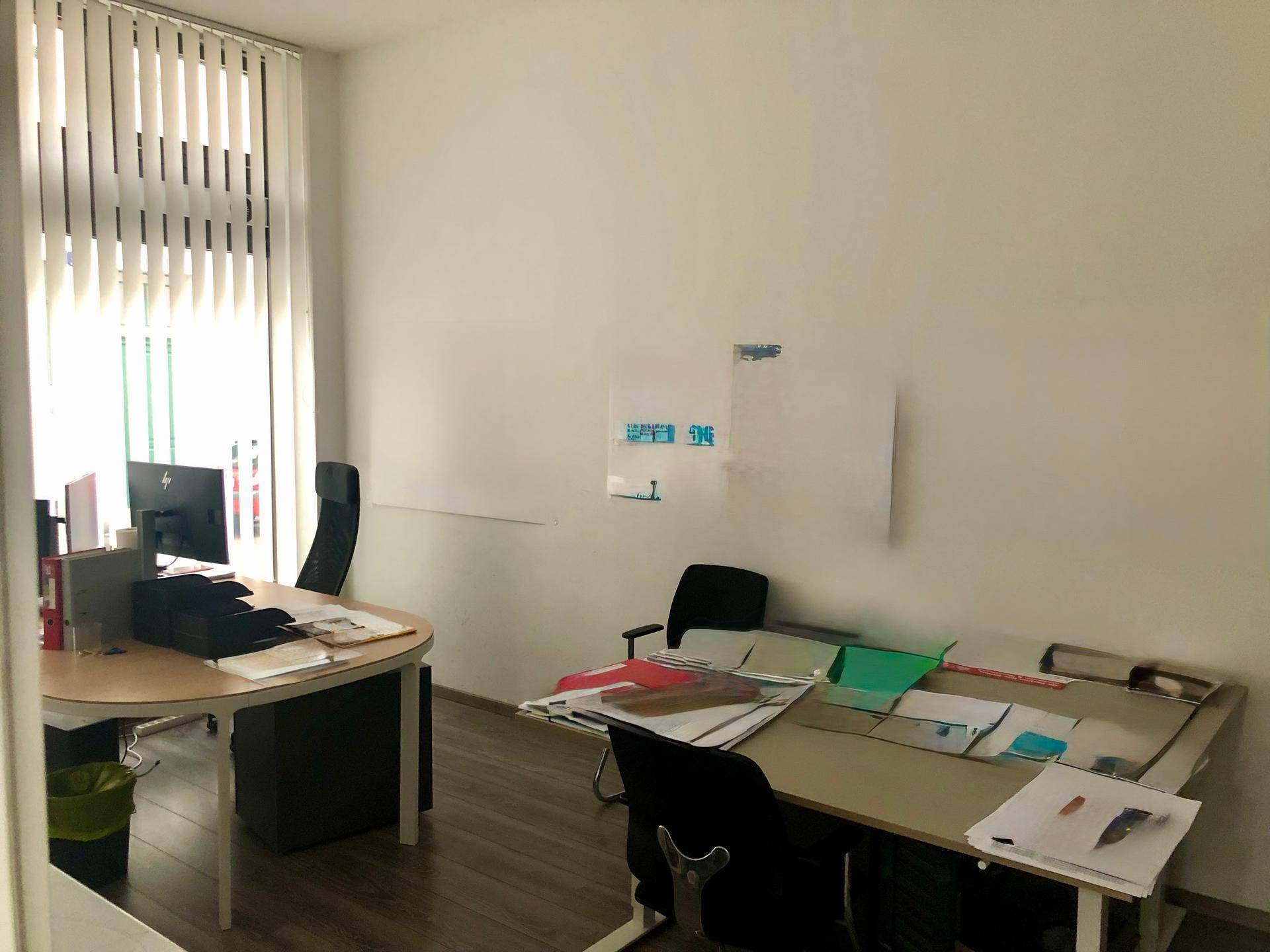 Geräumiges Büro mit zwei Schreibtischen, Bürostühlen und vertikalen Jalousien am Fenster.