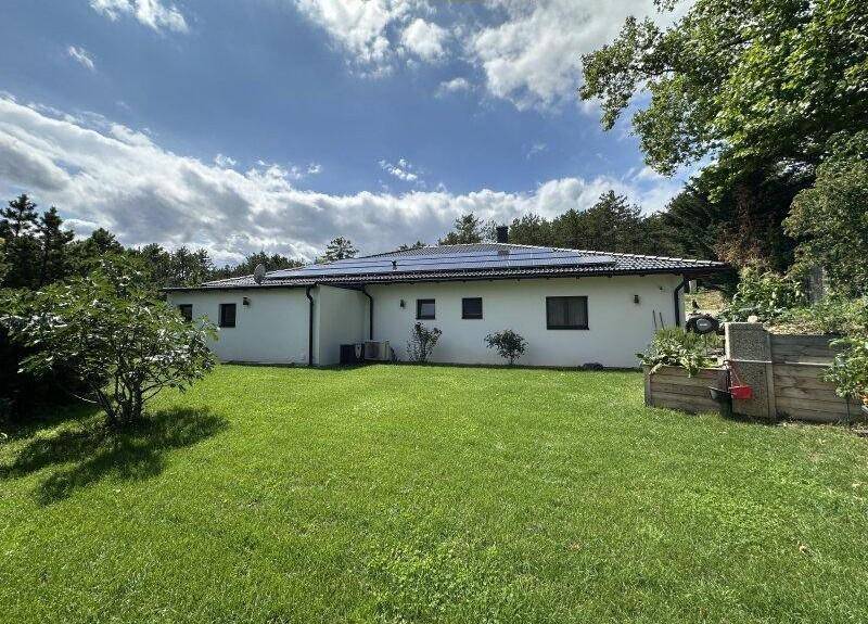 Rückseite des modernen Hauses mit weitläufigem Rasen und grüner Umgebung.