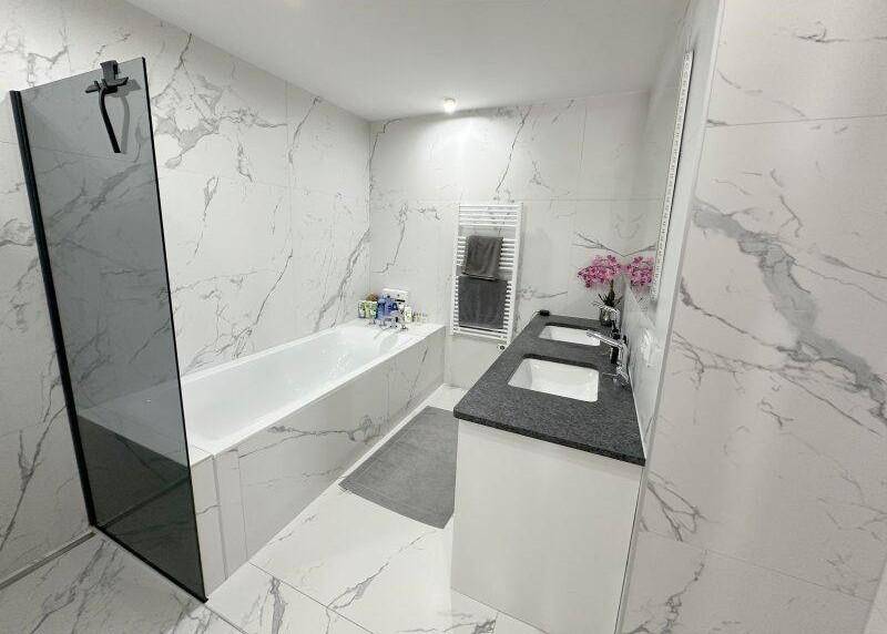 Elegantes Badezimmer mit Badewanne, Doppelwaschbecken und großformatigen Marmorfliesen.