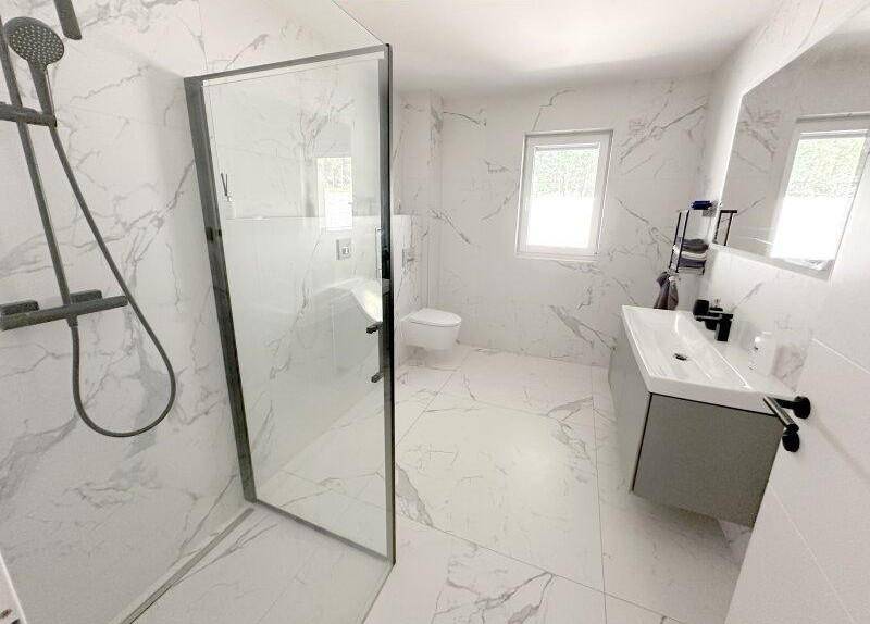 Elegantes Badezimmer mit begehbarer Dusche, wandhängendem WC, modernem Waschtisch und Fenster.