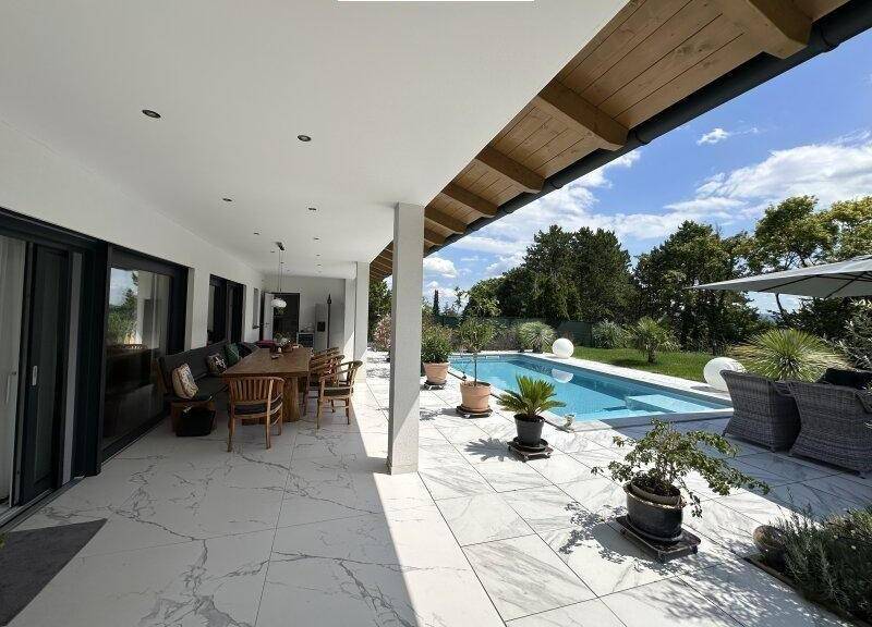 Überdachte Terrasse mit Essbereich und Blick auf den Pool und den grünen Garten.