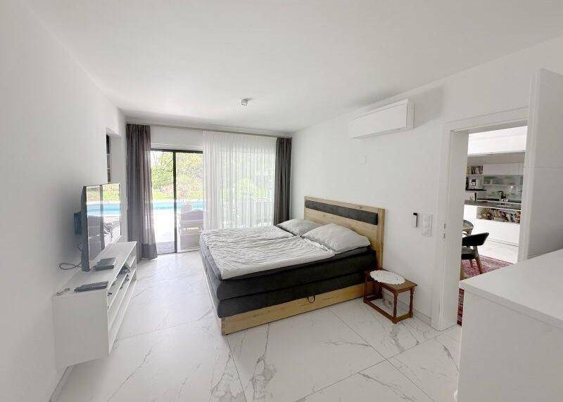 Helles Schlafzimmer mit großem Bett, Fliesenboden, Klimaanlage und direktem Zugang zum Poolbereich.