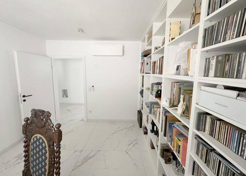 Helles Arbeitszimmer mit raumhohen Bücherregalen und Klimaanlage.