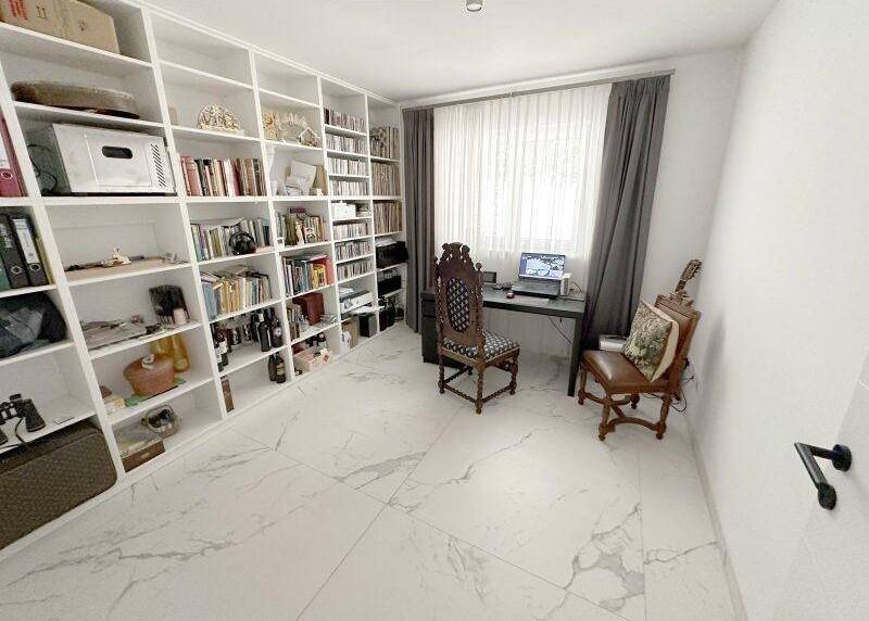 Gemütliches Arbeitszimmer mit umfangreicher Bibliothek, Schreibtisch und Fenster.