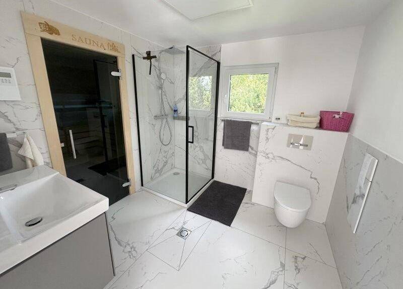 Modernes Badezimmer mit Dusche, WC, Waschtisch, Fenster und integrierter Sauna für Wellness.