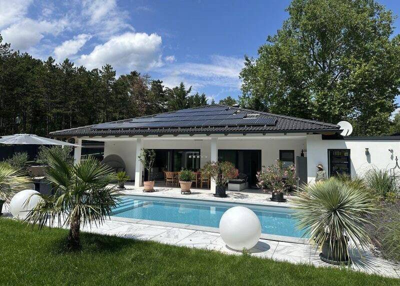 Weitläufiger Gartenbereich mit Pool und moderner Villa unter strahlend blauem Himmel.