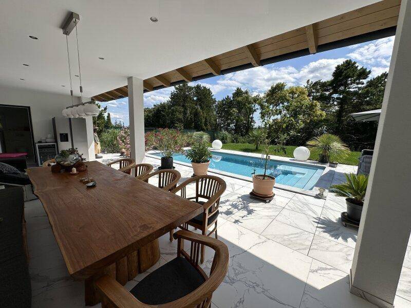 Großer Holztisch auf der überdachten Terrasse, ideal für Mahlzeiten im Freien mit Poolblick.