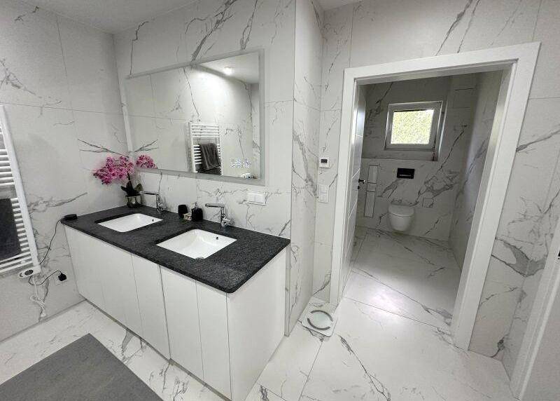 Modernes Badezimmer mit Doppelwaschbecken, Marmorfliesen und separatem WC-Bereich.