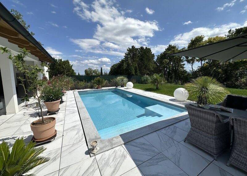 Moderner Poolbereich mit weiß gefliestem Terrassenboden und bequemen Gartenmöbeln.