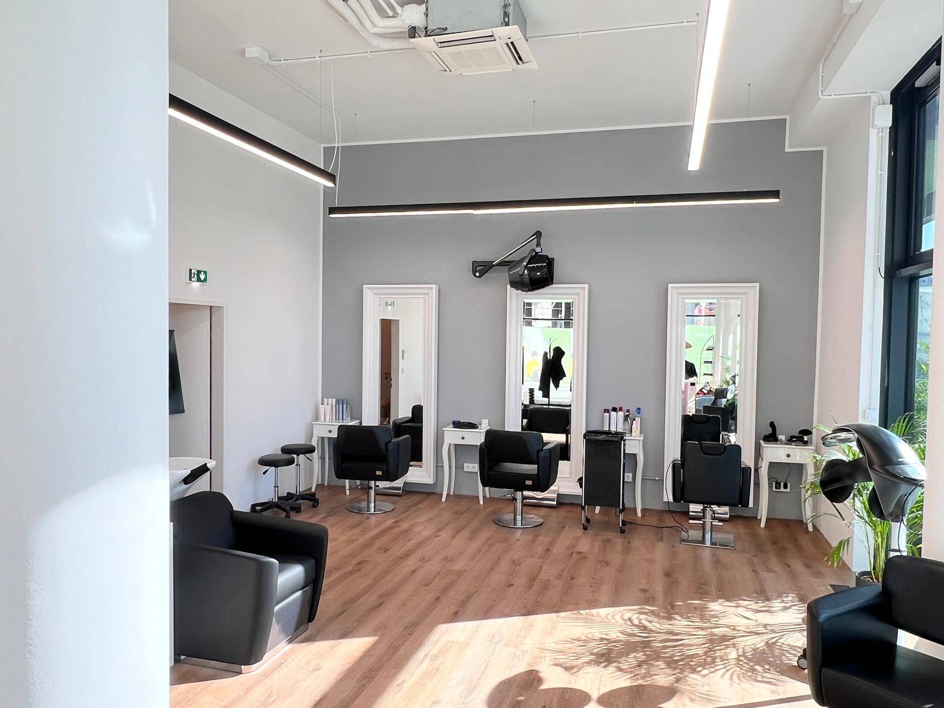 Heller und moderner Friseursalon mit mehreren Bedienplätzen, großen Spiegeln, Holzboden und viel Tageslicht.