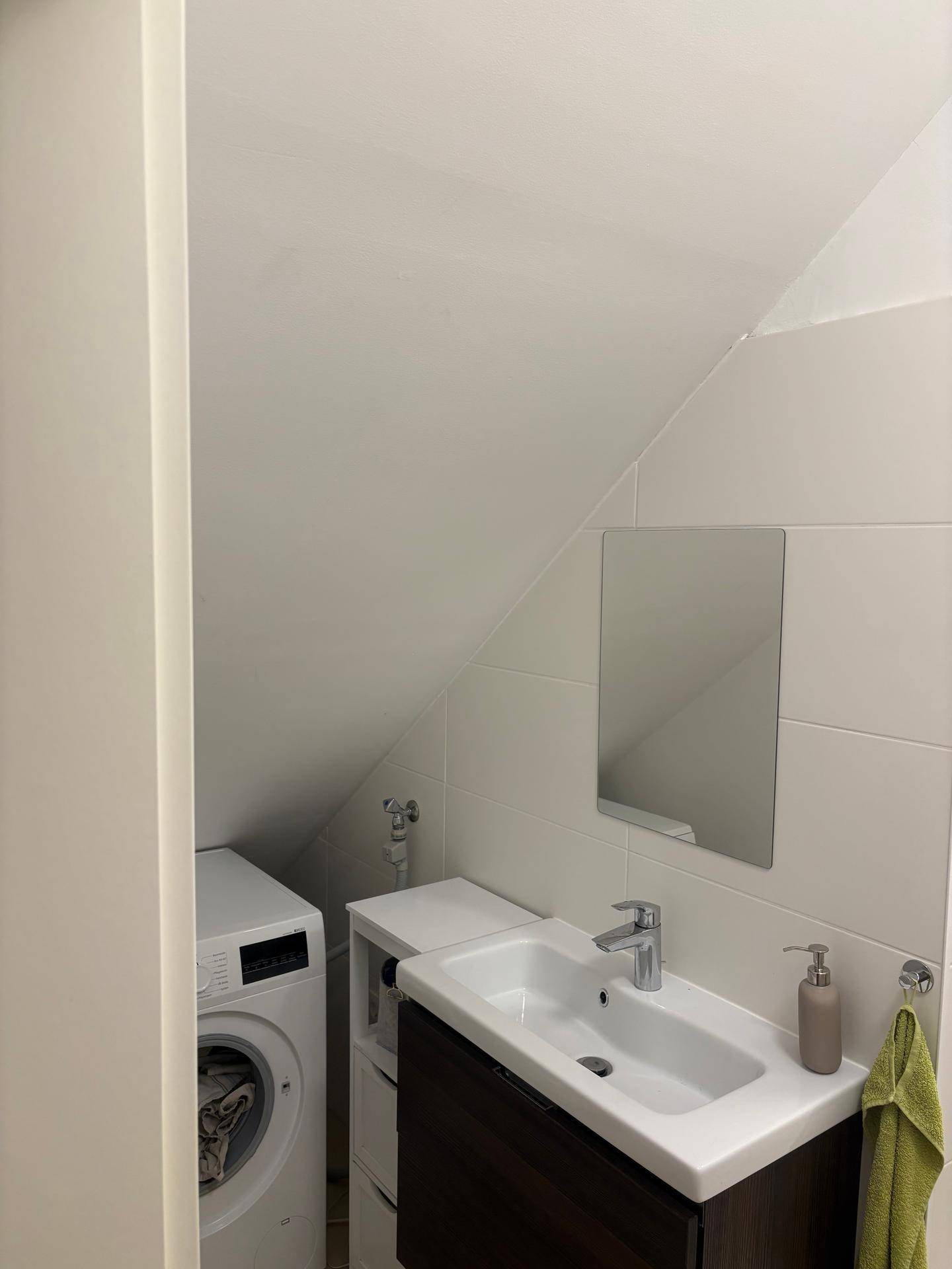 Badezimmer mit Waschbecken, Spiegel und Waschmaschine unter einer Dachschräge, praktisch eingerichtet.