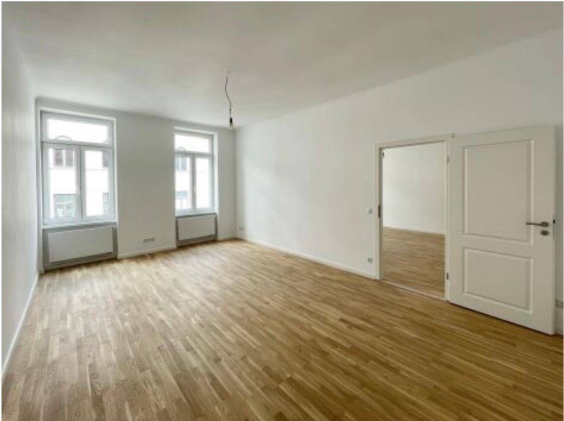 Geräumiges, helles Zimmer mit Holzboden und zwei großen Fenstern, bereit zur Einrichtung.