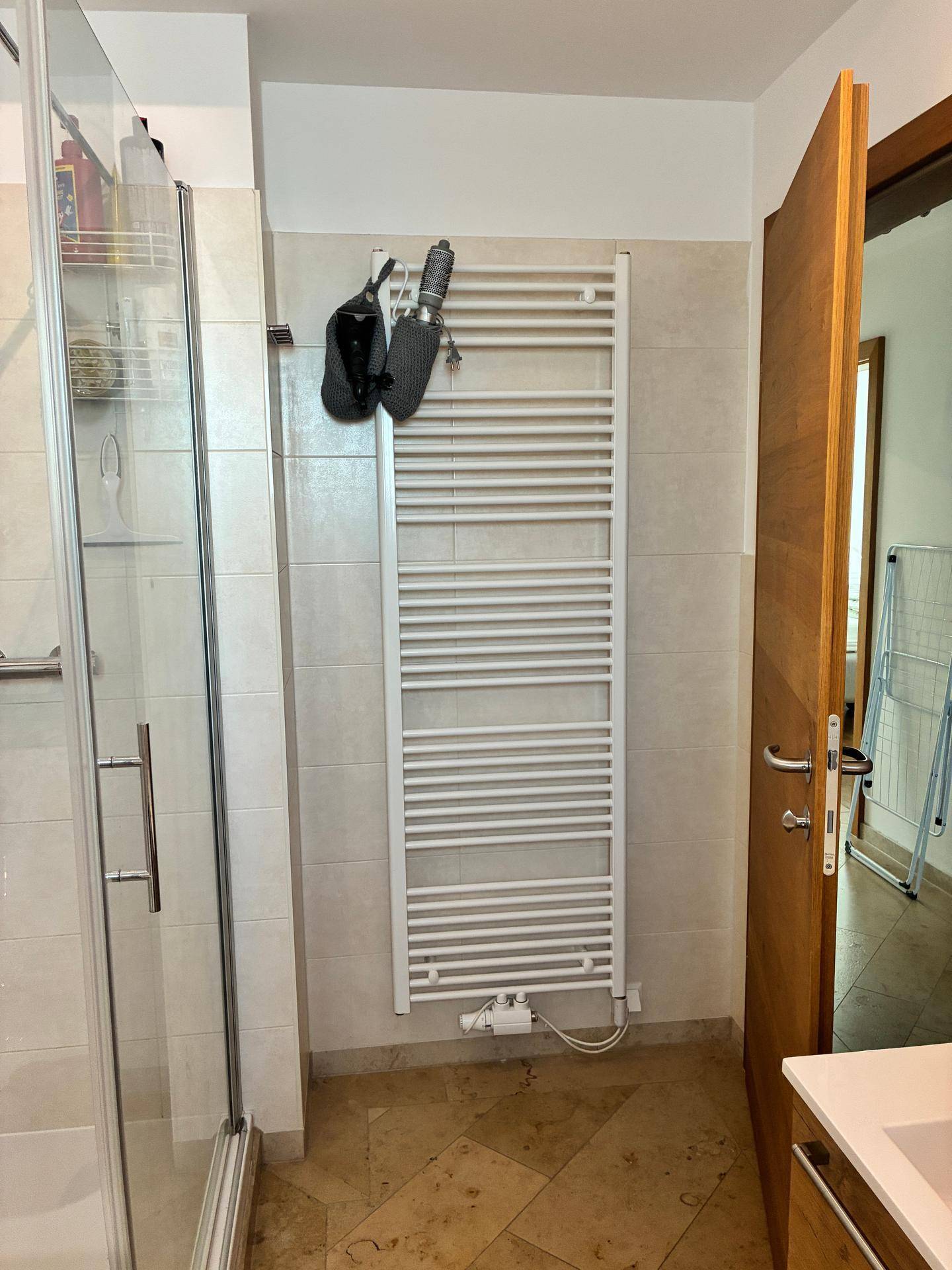 Badezimmer mit Duschkabine, Handtuchheizkörper und beigen Fliesen.
