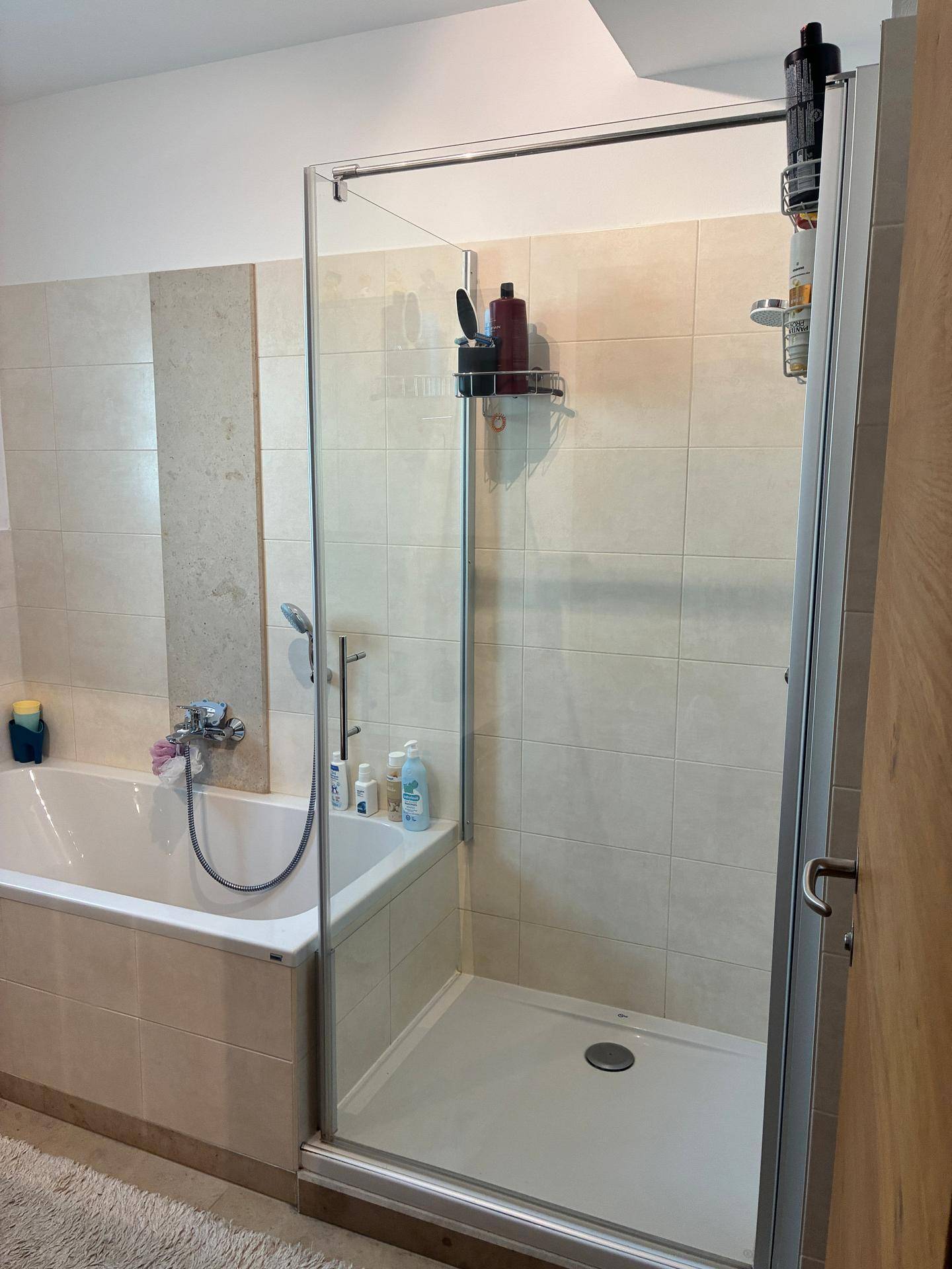 Badezimmer mit Badewanne, Duschkabine und beigen Wandfliesen.
